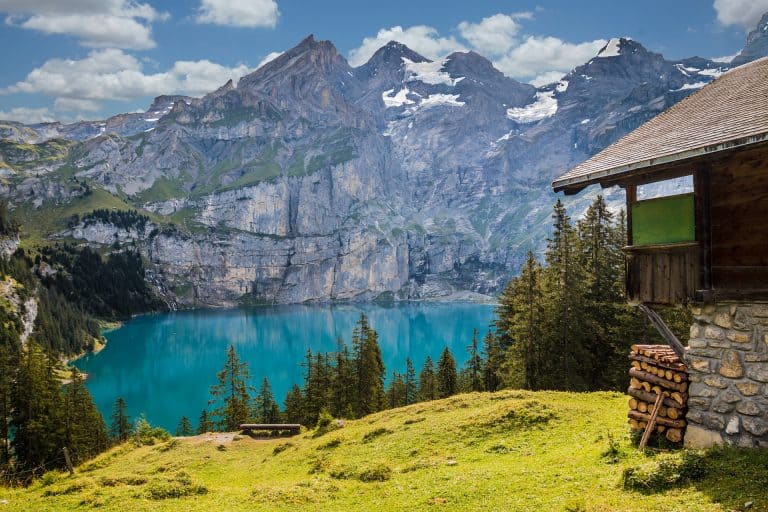a photo of a cabin on a lake in switzerland with the mountains in the background.