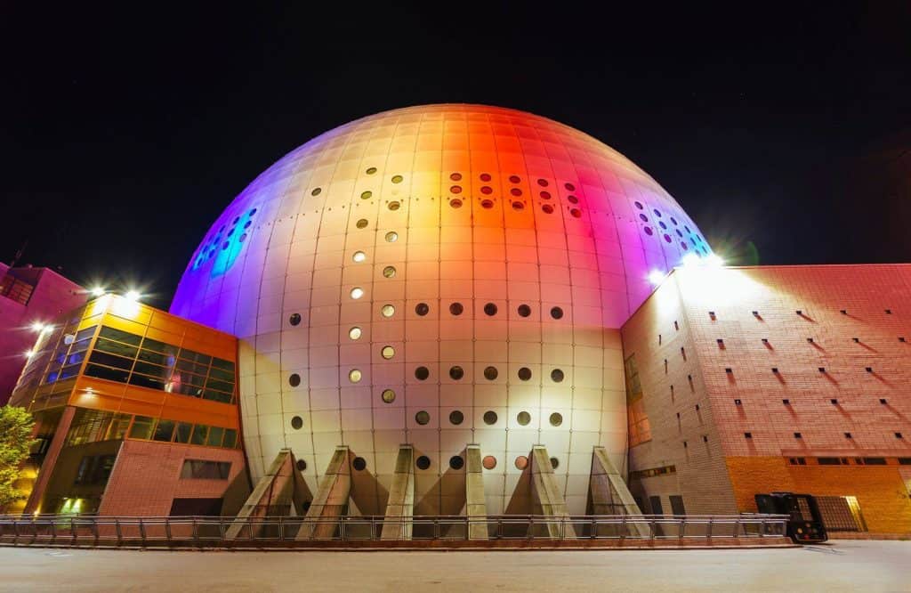 A colorful dome at night that's lit up and is known as the Avicii Arena