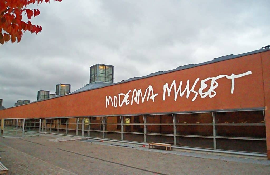 A brown building with white graffiti on it saying "Moderna Museet."