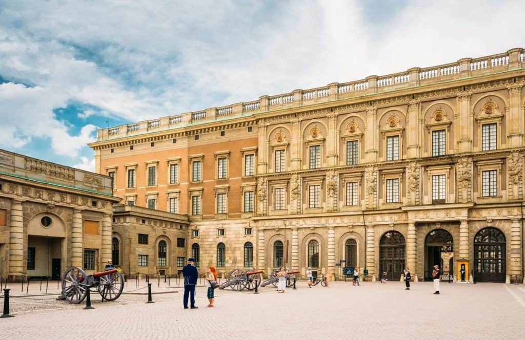 A tan and light brown building with an elegant look and a few people admiring it known as the Royal Palace