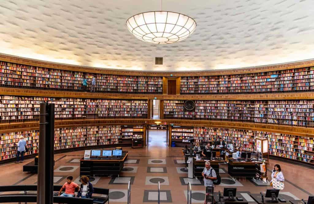 A curved bookshelf covered in books and an opulent chandelier in the middle of the room