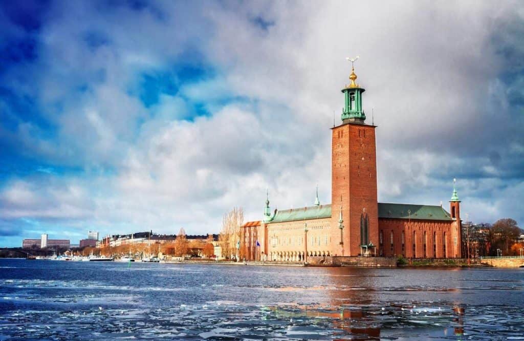 A brown building on the water with a tower that's known as Stockholm City Hall
