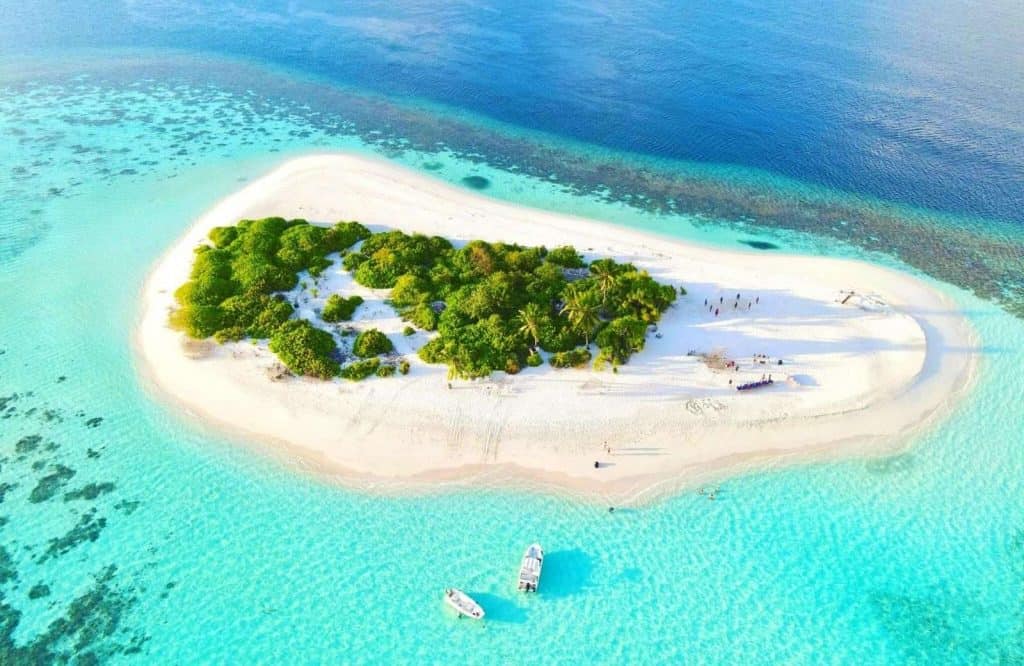 A small island nestled in the Indian Ocean and surrounded by stunning light blue water.