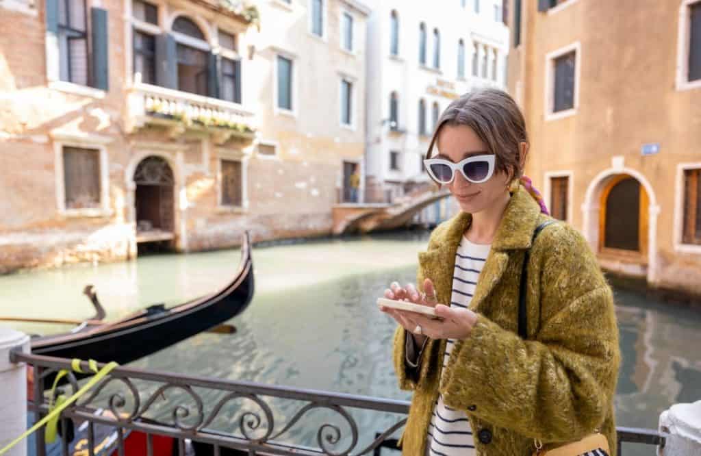 A girl off to the side of the street looking at her phone in Venice and getting out of the way is one of the best things to know before visiting Venice.