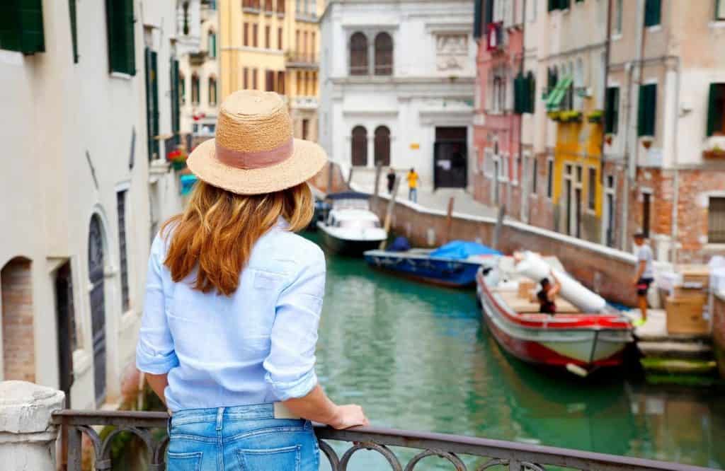 A girl standing on a bridge overlooking the canal, one of the best things to know when visiting Venice is how expensive it is.