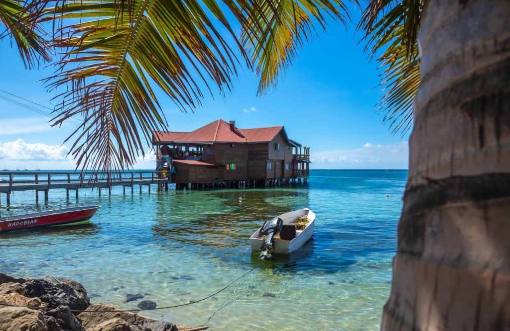 A palm tree framing a photo of a building out on the ocean in West End, which belongs on every one day in Roatan itinerary.