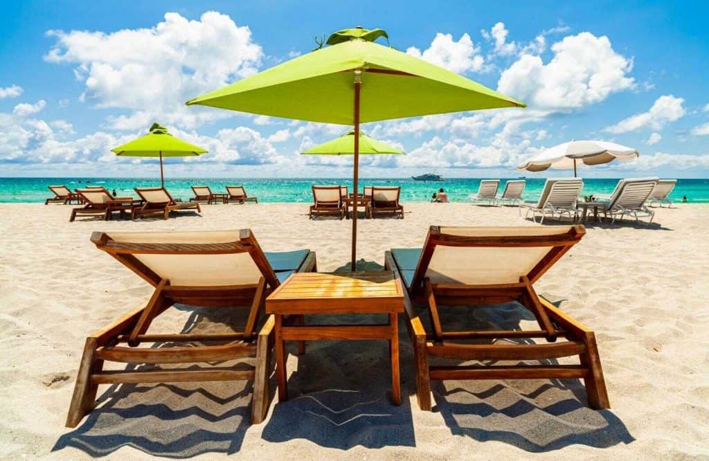 Two beach chairs and a green umbrella on a beach in Miami.