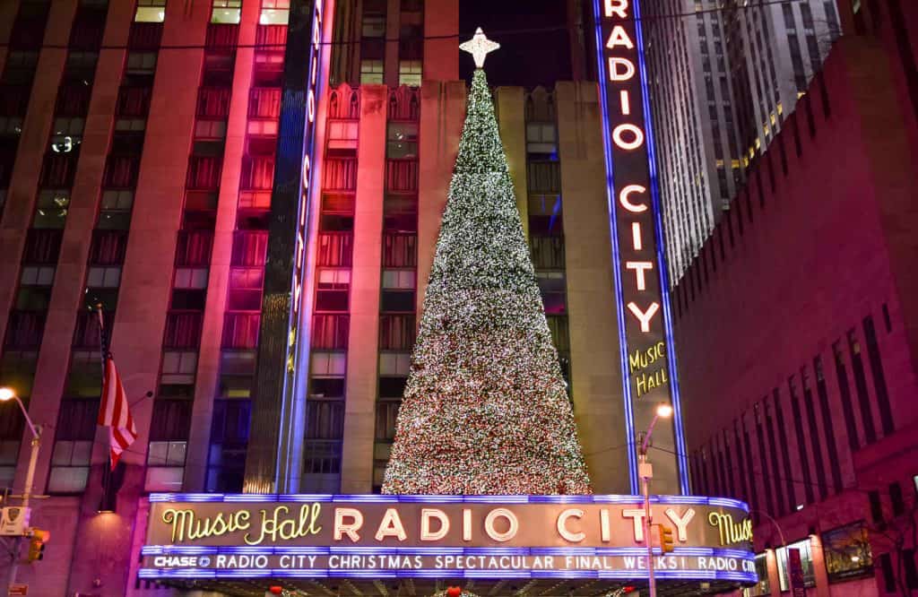 Lit up giant Christmas tree on top of the Radio City Music Hall sign.
