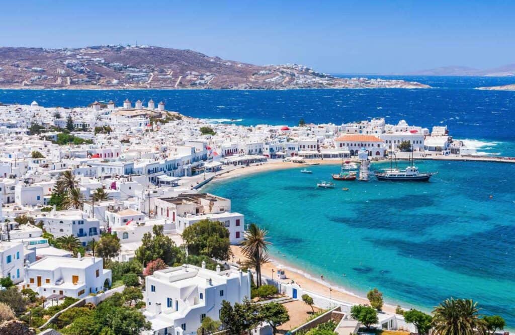 Aerial view of the island of Mykonos with clear blue water and white picturesque buildings.