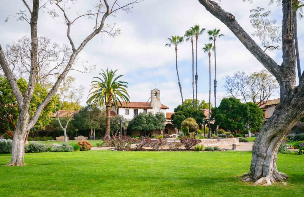 The exterior of Mission San Juan Capistrano on a lush green garden with trees.