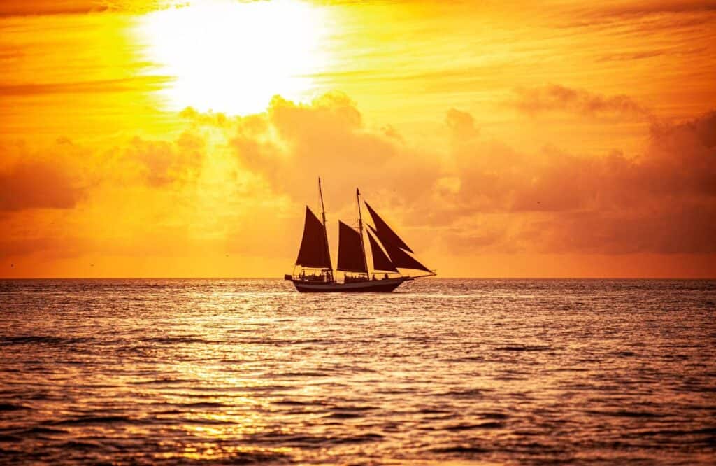 A fiery sunset with orange skies with a schooner boat on the water for the best sunset cruise in Key West.