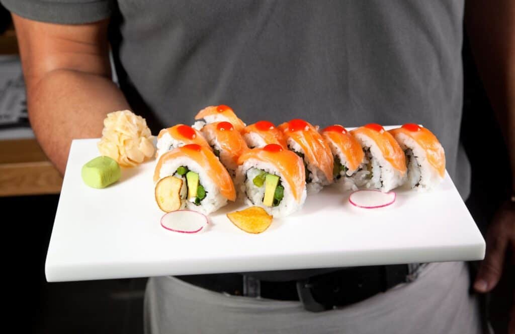 A man holding a plate of sushi with wasabi and ginger.