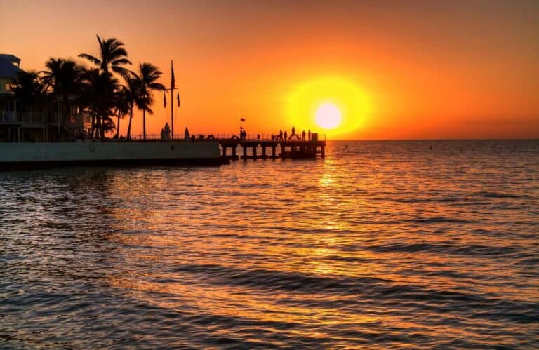 A sunset with bright orange skies behind a pier on the water, which is perfect for sunset cruises in Key West.