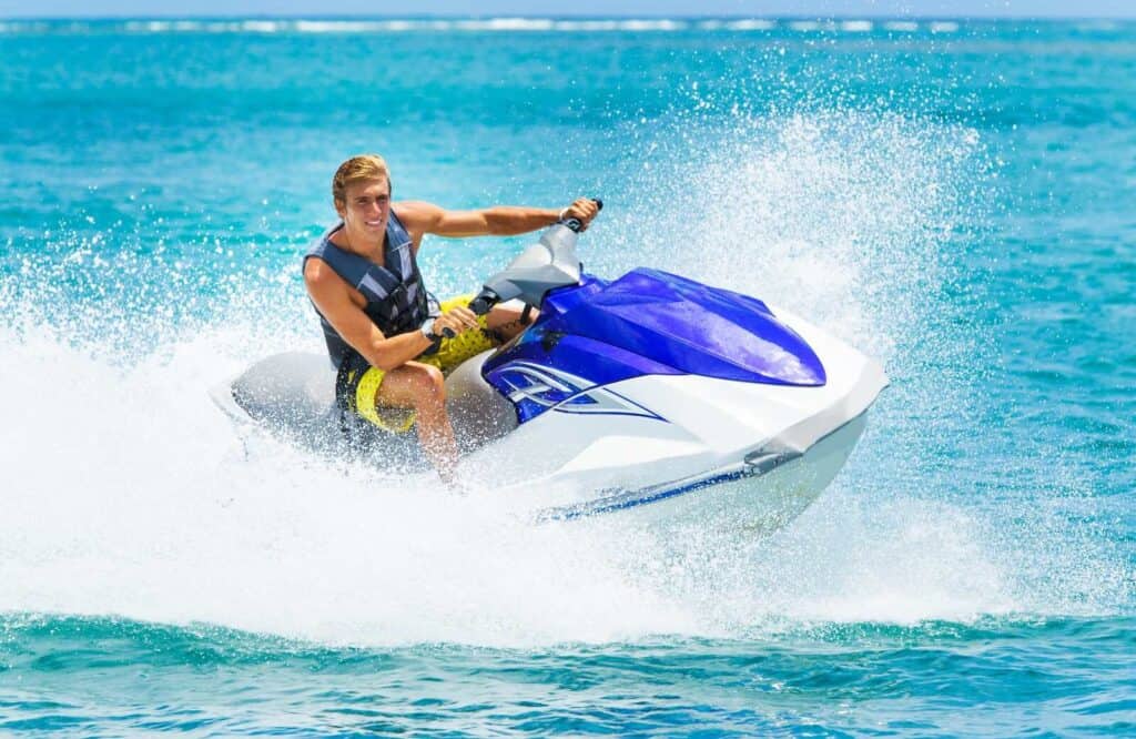A man in yellow shorts on a blue and white jetski on one of several dolphin tours in Destin.
