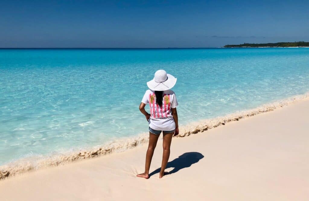 A woman wearing a white sunhat standing on the beach in the Bahamas.
